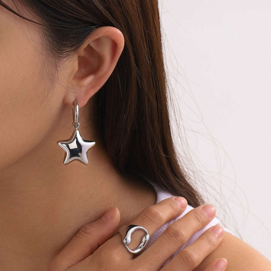 Star-shaped silver earring worn by a person with a plain background