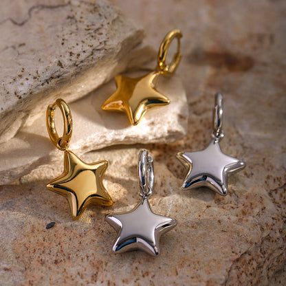 Star-shaped earrings in gold and silver on a stone surface