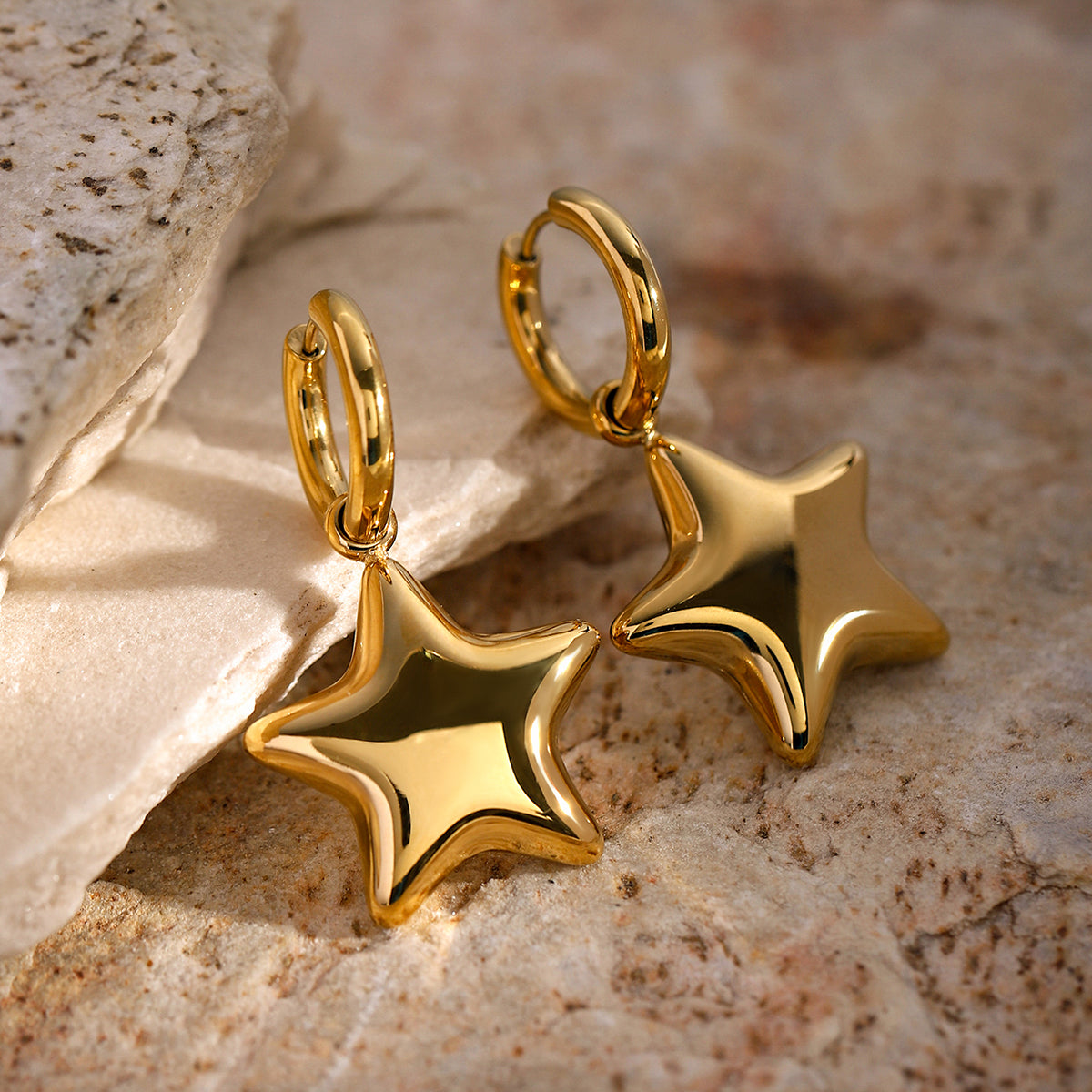 Gold star-shaped earrings on a textured stone surface