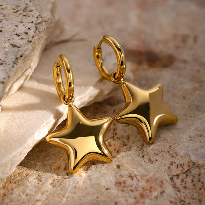 Gold star-shaped earrings on a textured stone surface