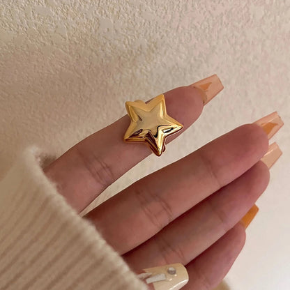 Gold star-shaped ring on a finger against a neutral background