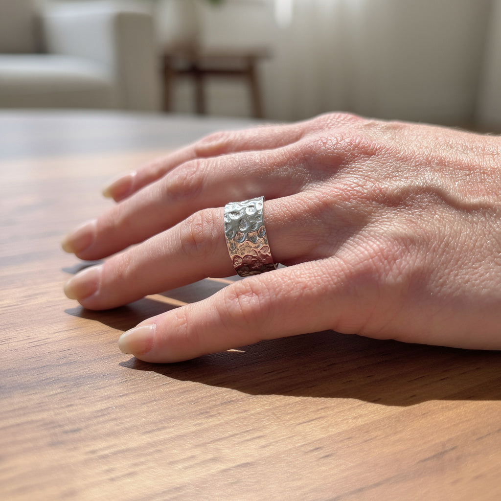 Hand wearing a silver ring on a wooden surface with a blurred indoor background