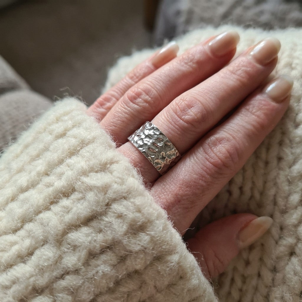 Hand wearing a silver ring with textured band, holding a beige knitted fabric.
