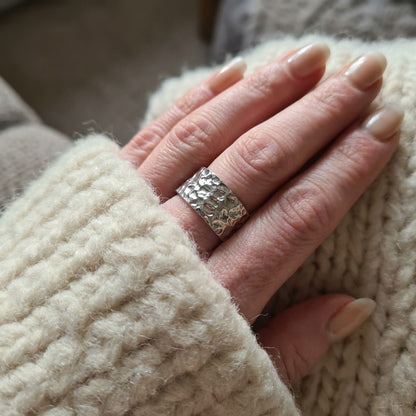 Hand wearing a silver ring with textured band, holding a beige knitted fabric.