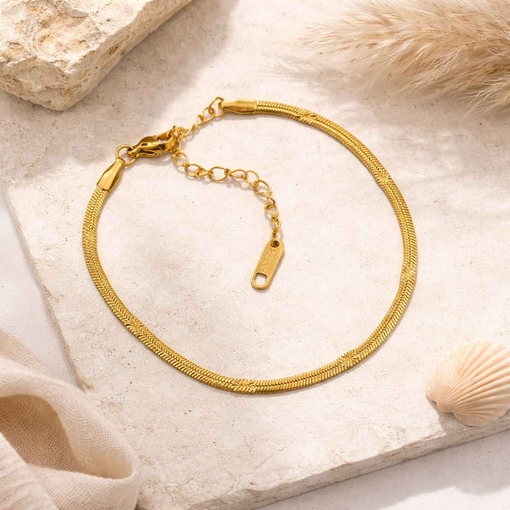 Gold bracelet on a textured stone surface with a shell and fabric