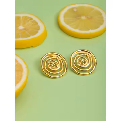 Gold spiral earrings on a green background with lemon slices.