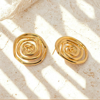 Gold stainless steel spiral earrings on a textured beige surface