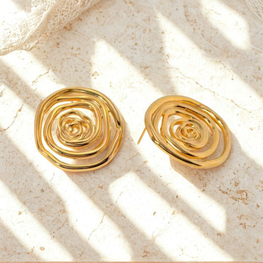 Gold stainless steel spiral earrings on a textured beige surface