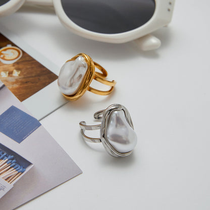 Two chunky rings with pearl-like stones on a surface with a magazine and sunglasses in the background.