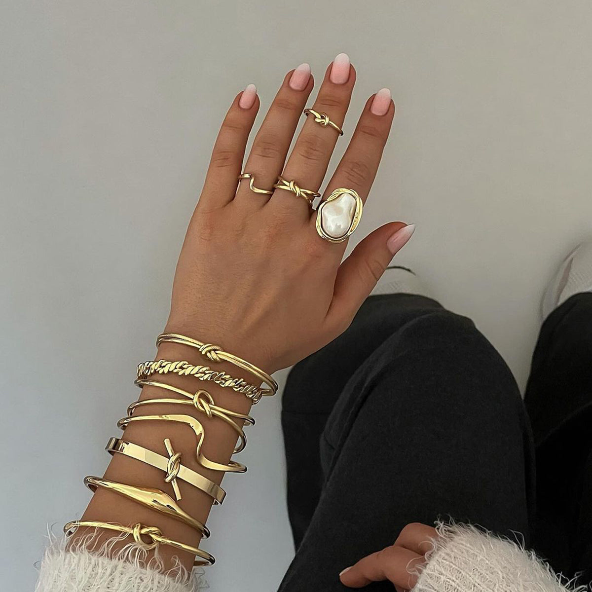 Hand wearing multiple gold rings and bracelets on a neutral background