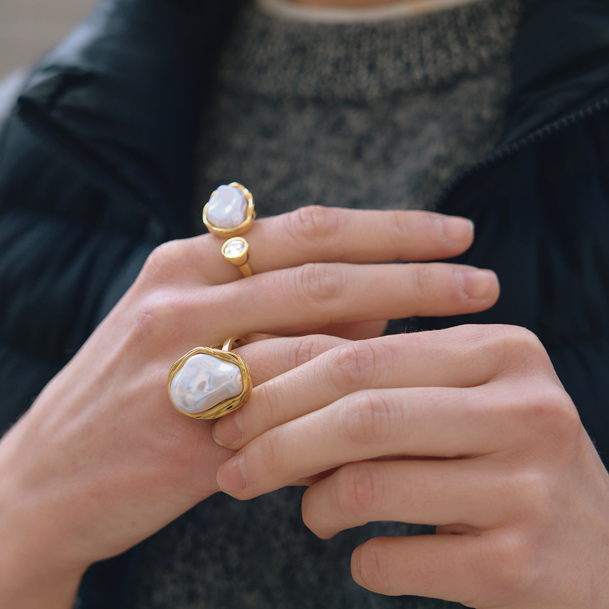 Close-up of hands wearing gold chunky rings with large white stones.