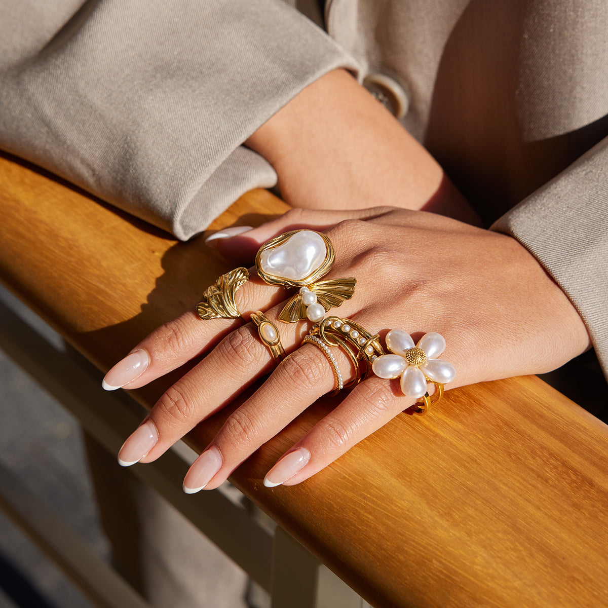 Close-up of a hand wearing gold rings with pearl accents on a wooden surface.
