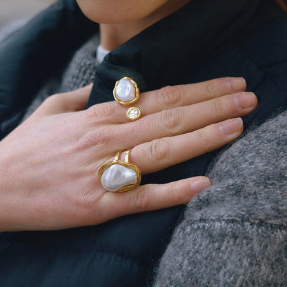 Close-up of a hand wearing statement gold rings with pearl-like stones on a dark background