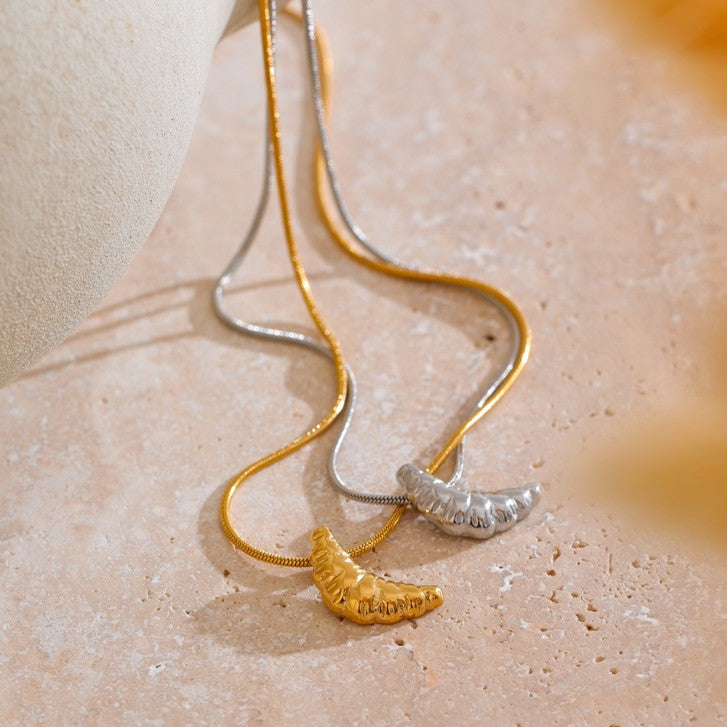 Two necklaces with croissant-shaped pendants on a beige surface