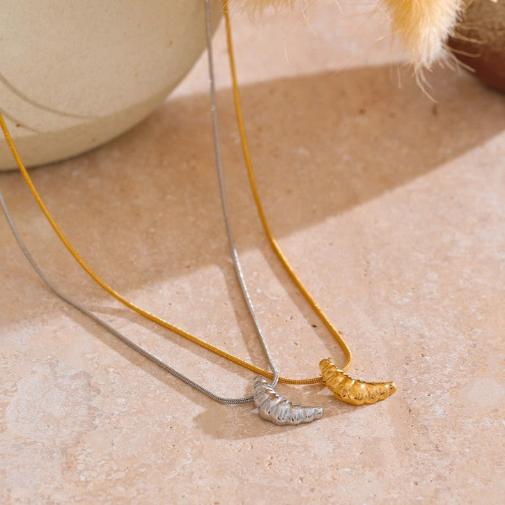 Two gold and silver stainless steel necklaces with unique pendants on a beige surface.