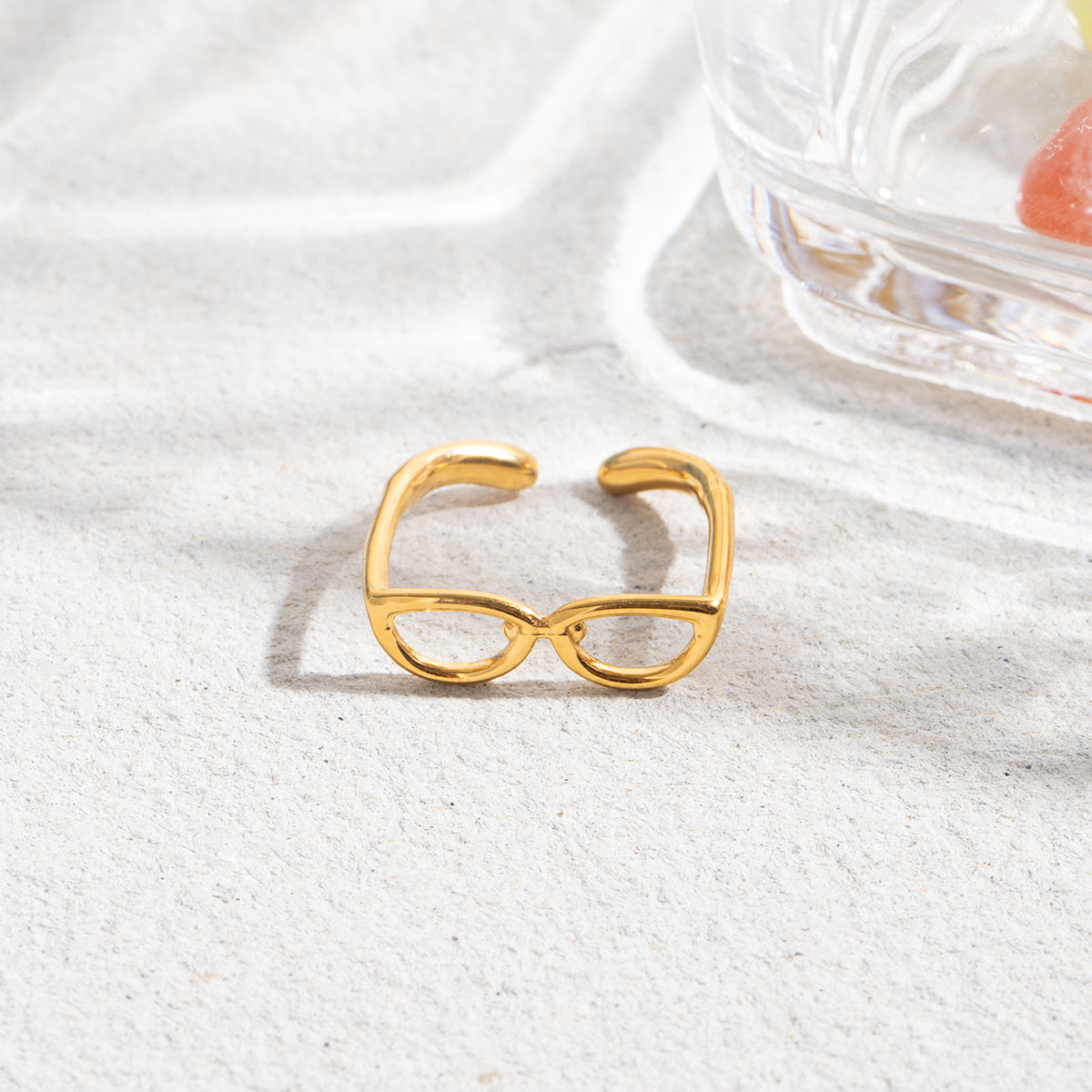 Gold eyeglass-shaped ring on a white fabric background