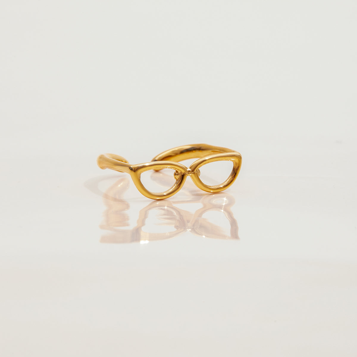 Gold eyeglass-shaped ring on a light gray background