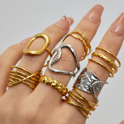 Hand wearing multiple gold and silver rings on a neutral background