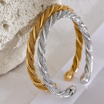 Two braided gold and silver bracelets on a textured surface