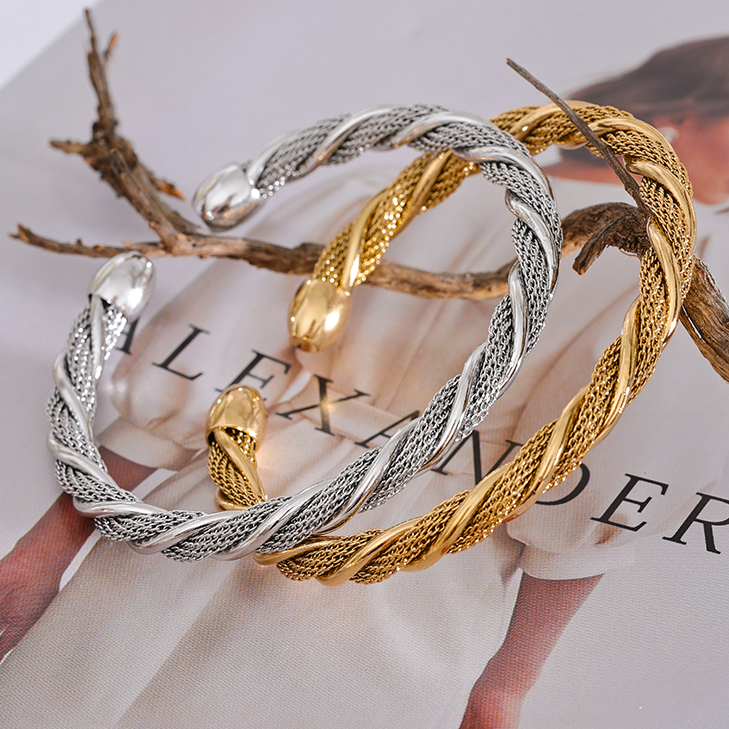 Two twisted stainless steel bangles, one silver and one gold, on a magazine page.