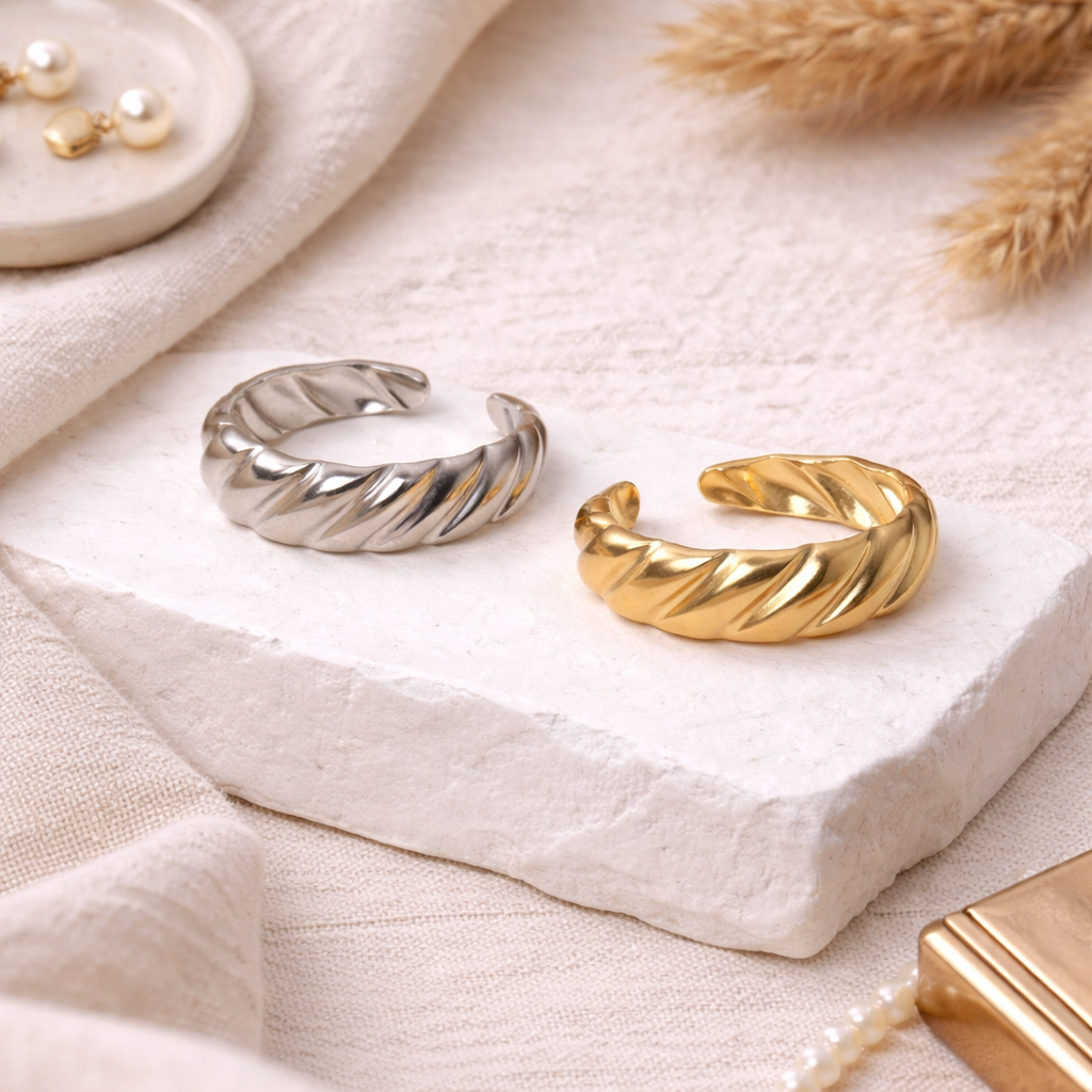 Gold and silver rings on a textured white surface with dried grasses in the background.