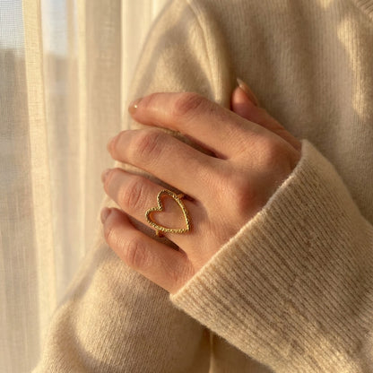 Hand wearing a gold heart-shaped waterproof ring with a soft, blurred background